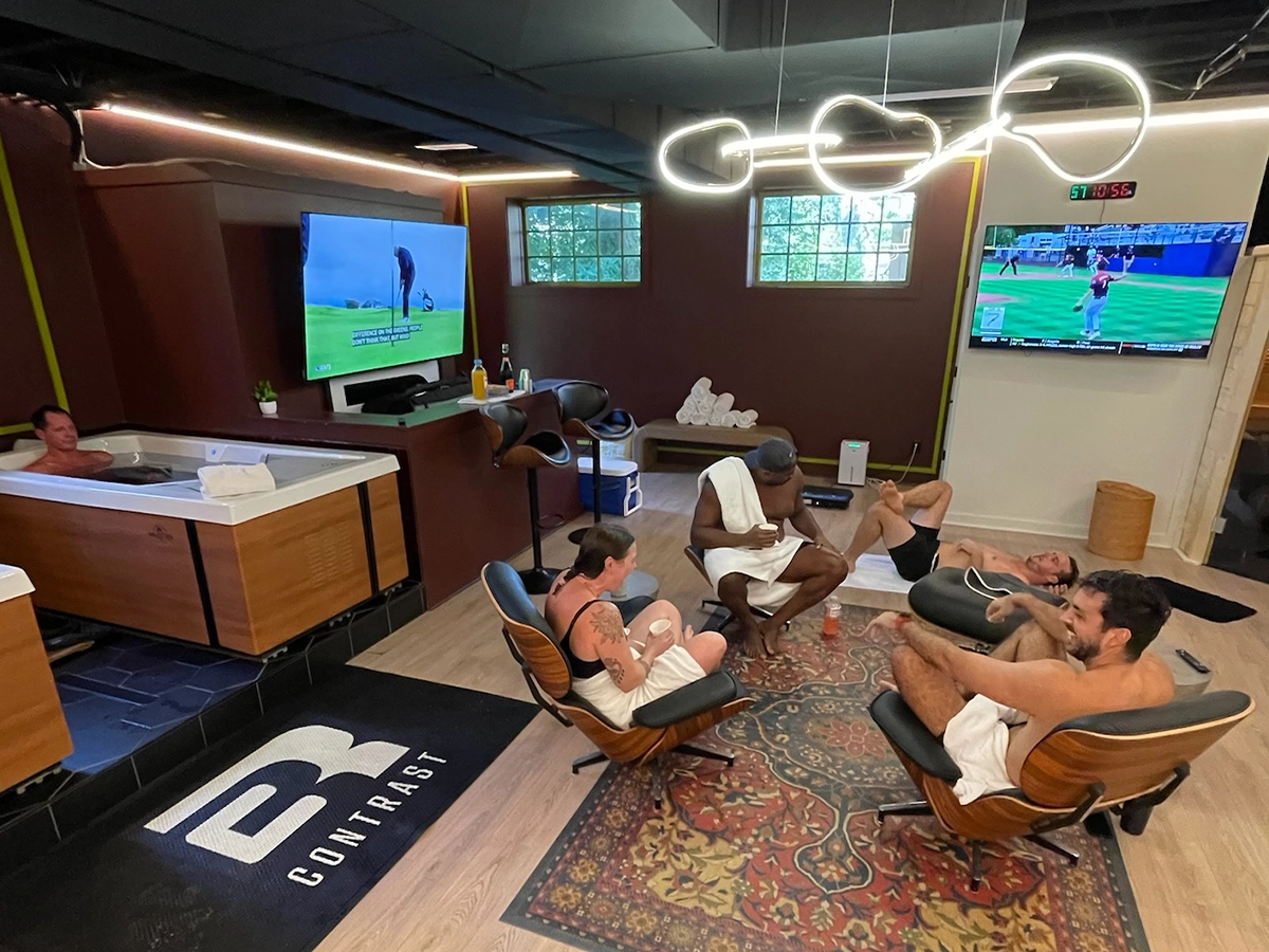 Members unwinding in lounge chairs and the hot tub while watching TV in the R3 Contrast recovery lounge