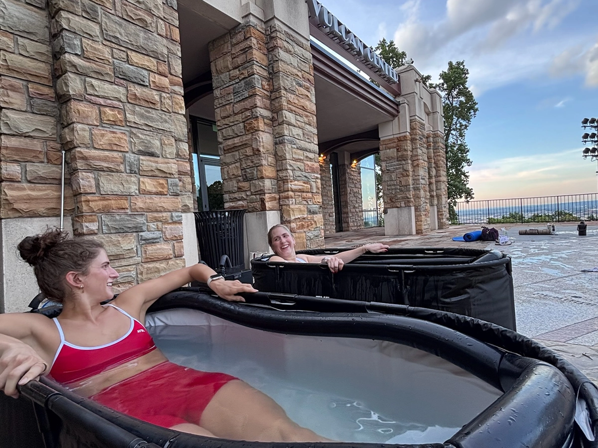 Two women laughing in portable cold plunge tubs at an R3 Contrast pop-up event at Vulcan Park